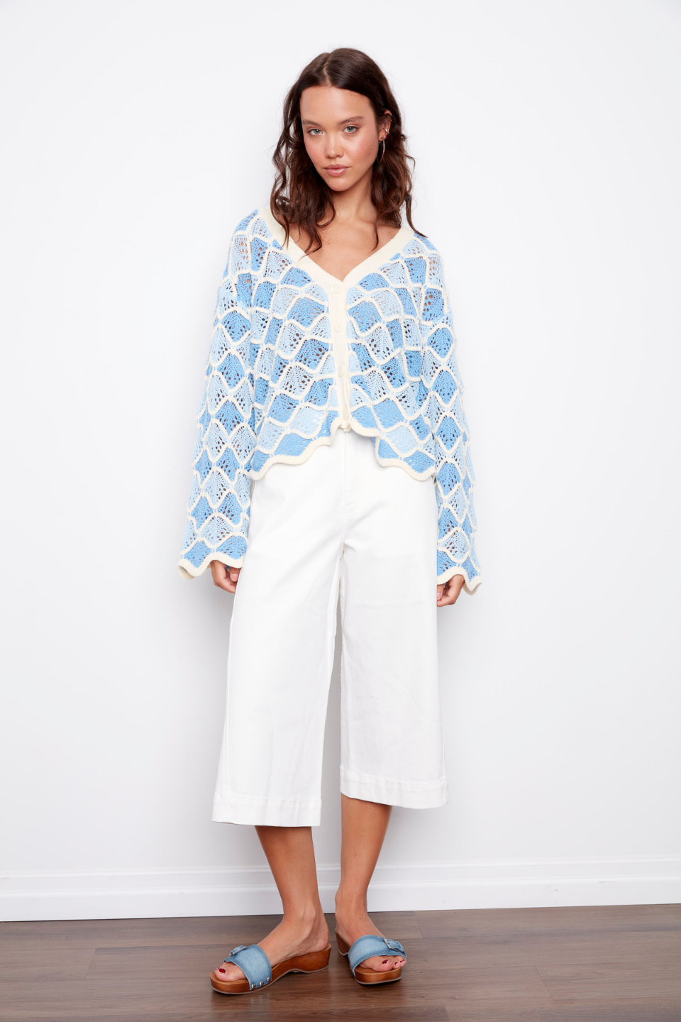 Woman wearing a blue patterned cardigan over a white top and pants on a white background